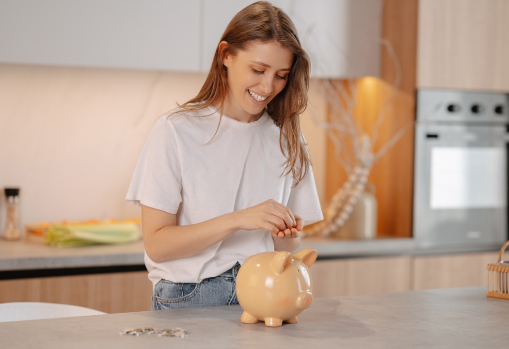A young lady saving money and putting coins into her piggy bank