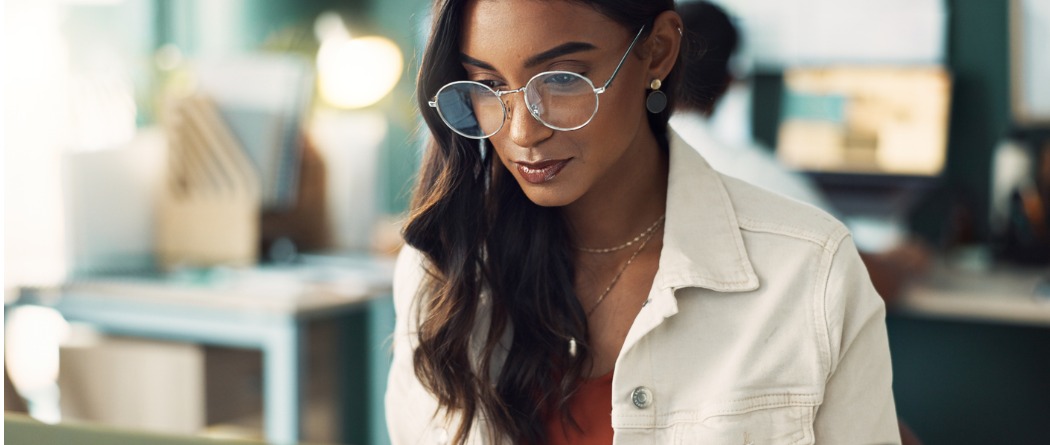 A woman wearing a white jacket and glasses looking at a computer