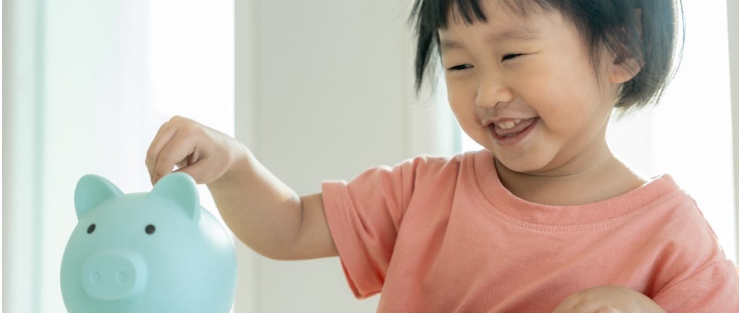 A young girl is putting money into her blue piggy bank. 
